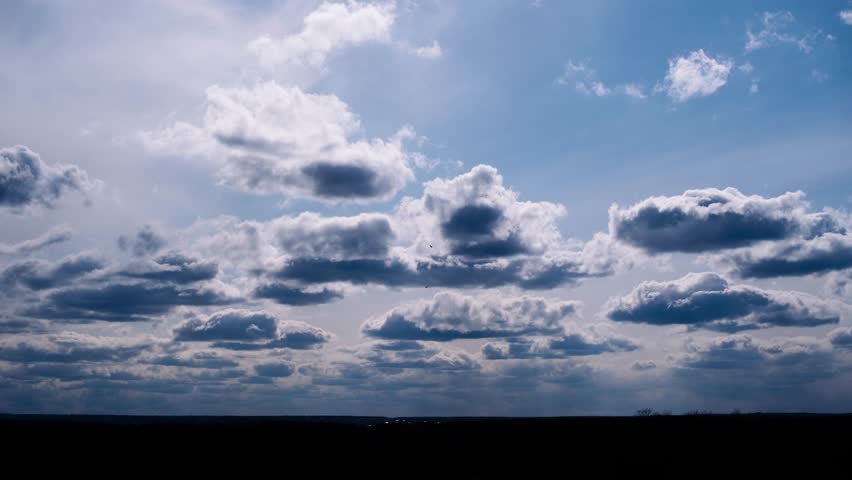Wide-angle timelapse shows puffy cumulus clouds drifting across bright blue sky, casting shadows on a dark horizon below.