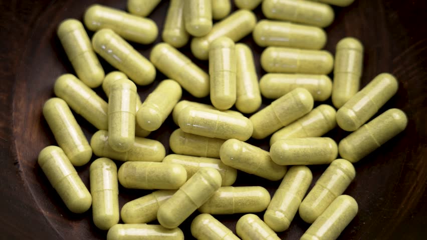 Green pharmaceutical painkiller capsules in a wooden bowl. Top view. Rotation