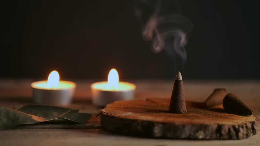 Incense is burning on a wooden stand, creating a calming atmosphere. Two candles flicker softly in the background, enhancing the tranquil setting as smoke wafts upward.