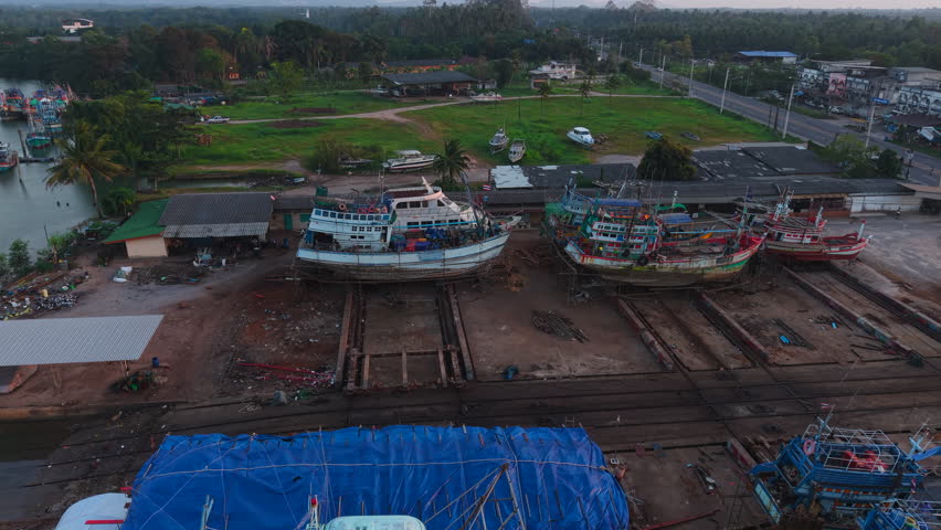 fishing boats in a shipyard near a road in a rural area at sunset