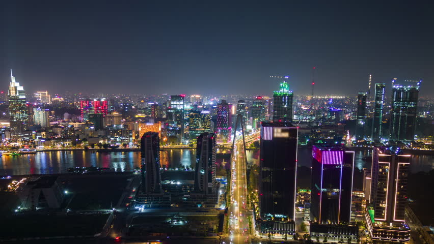 Timelapse aerial view of Ho Chi Minh City (Saigon), Vietnam, at night with glowing skyline, illuminated skyscrapers, and traffic lights reflecting on the river