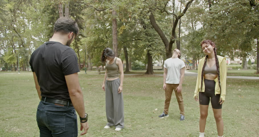 Students and their professor doing jumping jacks and other exercises in the park. They are smiling and look happy. Shot on Red Komodo 6k.