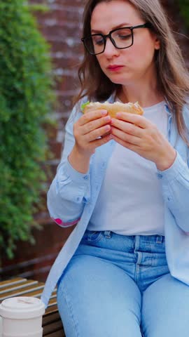 Woman having a lunch with a sandwich and coffee in the park with a laptop
