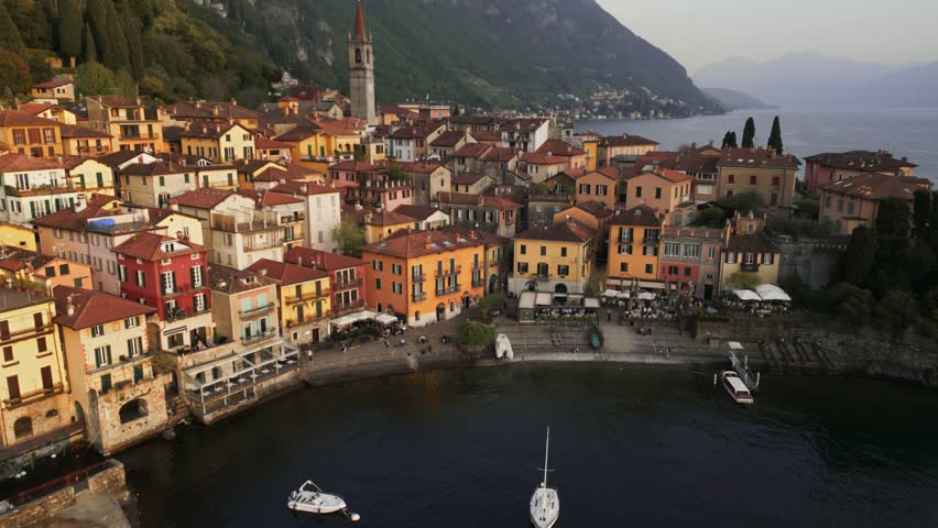 Aerial reveal dolly of Varenna during sunset, famous picturesque old town and turistic destination in Lake Como, Lombardy, Italy. Harbour in center shot. Golden hour. Cinematic 4K drone shot. 