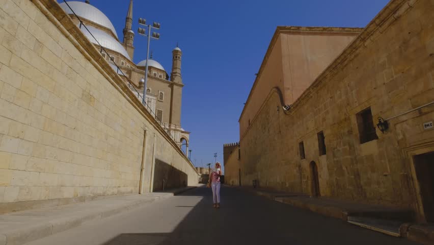 A woman walks down a historic street in Cairo, Egypt, with the grand mosque in the background. 