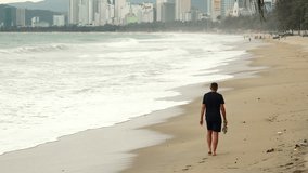 Back view of unrecognizable man in black clothes walks along beach with big waves. walk to refresh his thoughts and merge with nature. - Powered by Shutterstock - Get 15% off with code: PIKWIZARD15