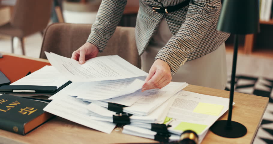 Person, hands and lawyer with documents for legal advice, testimonial or statements at office desk. Closeup, employee or attorney with paperwork for lawsuit, regulations or case notes at law firm