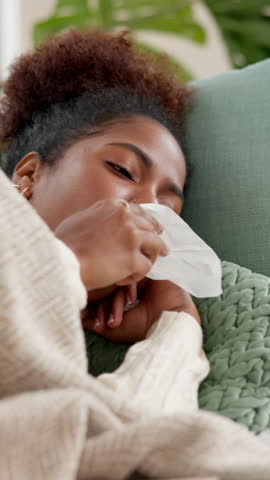 Sick, black woman and blowing nose with tissue for virus, disease or viral infection on sofa at home. Female person, cough or lying with influenza for sinus, hayfever or allergies on couch at house