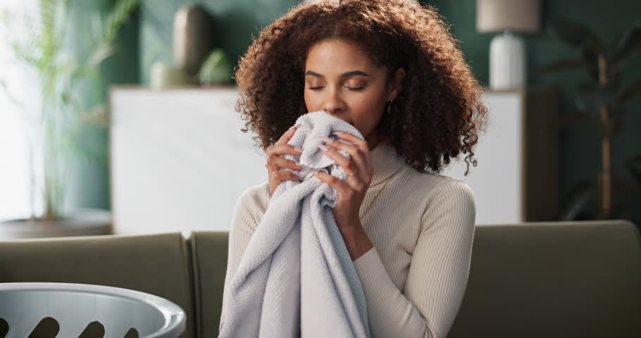 Woman, sofa and house or smell laundry, clean clothing and happy with fabric scent and washing basket in living room. Maintenance, aroma and fresh towel in apartment, satisfied and folding with smile