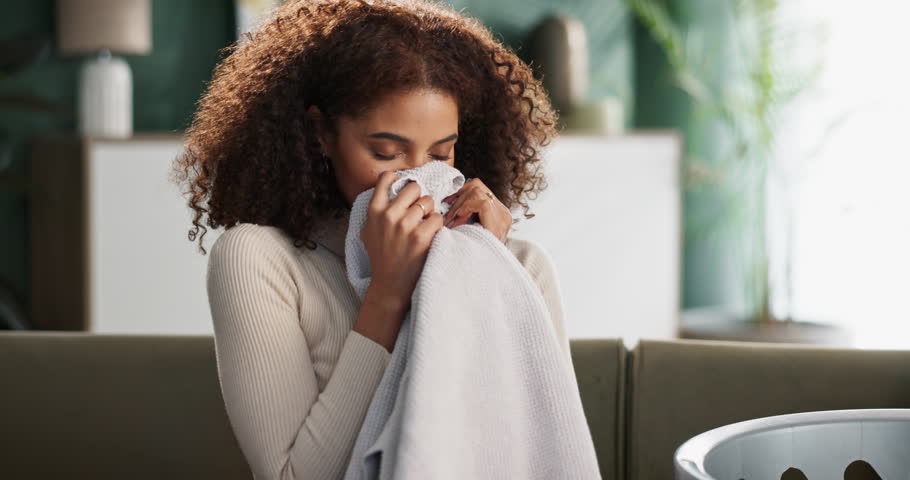 Woman, sofa and house or smell laundry, clean clothing and happy with fabric scent and washing basket in living room. Maintenance, aroma and fresh towel in apartment, satisfied and folding with smile