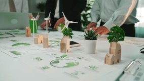 A diverse team collaborates on sustainable project planning, showcasing eco-friendly graphics and renewable energy concepts on their modern workspace table filled with plants and charts. SACTR - Powered by Shutterstock - Get 15% off with code: PIKWIZARD15