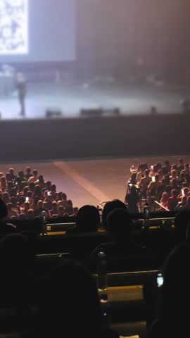 A large crowd of people are sitting in a theater. The audience is watching a performance on a large screen