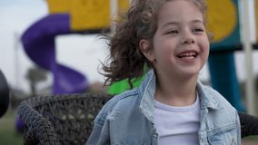Close-Up of Smiling Young Girl on Playground. Child girl with curly hair smiling while sitting on chair, outdoor - Powered by Shutterstock - Get 15% off with code: PIKWIZARD15