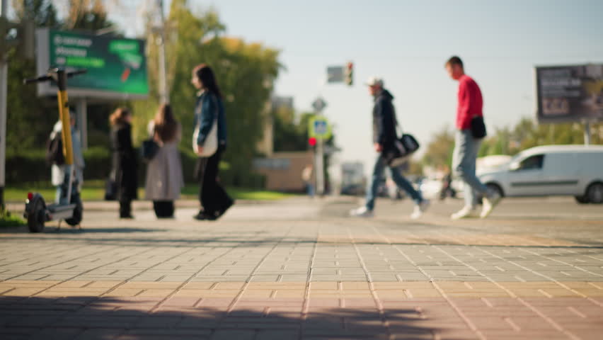 Blurred view of people walking on sidewalk with scooter in background, trees in the distance, urban scene during sunny day. Busy street with pedestrian movement and greenery around - Powered by Shutterstock - Get 15% off with code: PIKWIZARD15