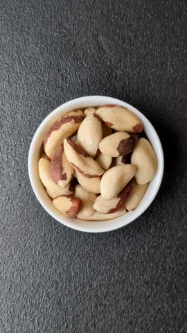 Brazil nut kernels in ceramic bowl on dark concrete background