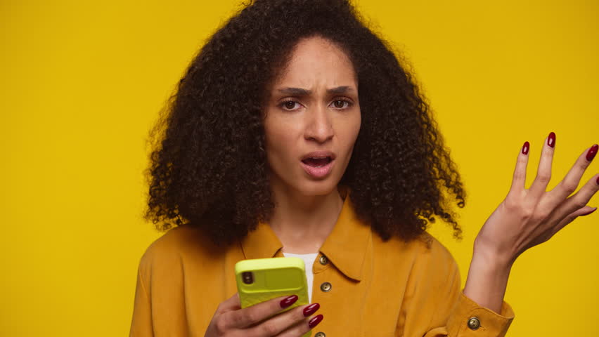 Frustrated woman reacting to smartphone message on yellow background