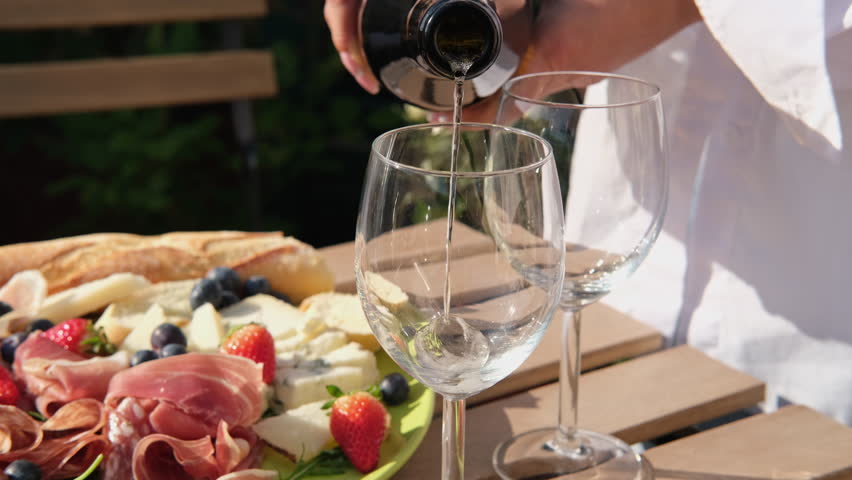 Pouring white wine or Prosecco into a glass from a bottle for an aperitif on the terrace 