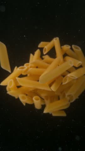 Super slow motion of falling uncooked italian pasta Penne into water, black background. Filmed on high speed cinema camera, 1000 frames per second.