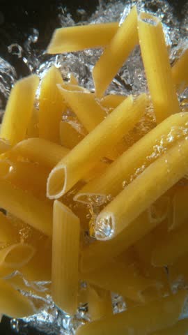 Super slow motion of falling uncooked italian pasta Penne into water, black background. Filmed on high speed cinema camera, 1000 frames per second.