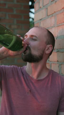 A depressed man drinks alcohol. The concept of alcohol addiction and homelessness. Vertical video.
