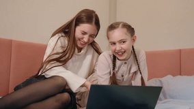 Young woman and little sister smiling while watching something on laptop together on bed. High quality 4k footage - Powered by Shutterstock - Get 15% off with code: PIKWIZARD15