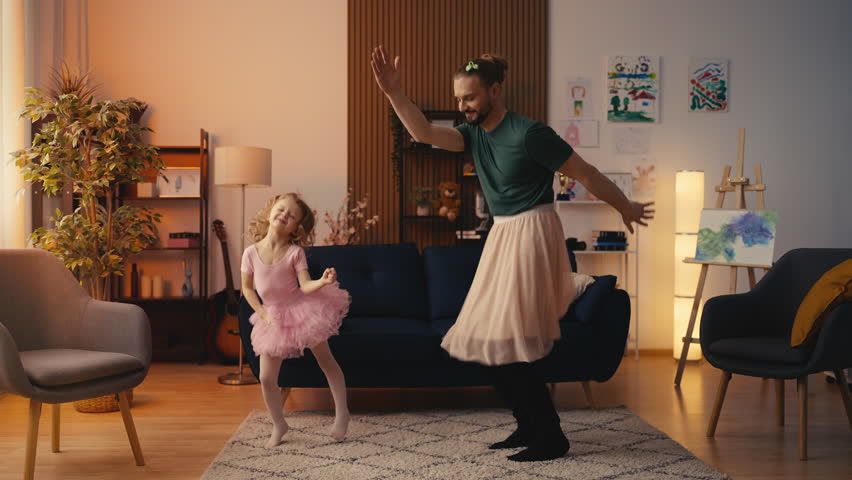 Happy little girl and father in pink skirts dancing together, fun family time