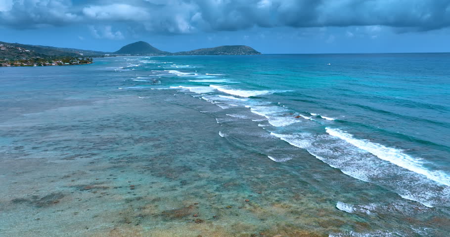 Low foamy waves roll to the coastline. Rainy clouds covering the sky. Pacific Ocean near the Hawaii, USA.