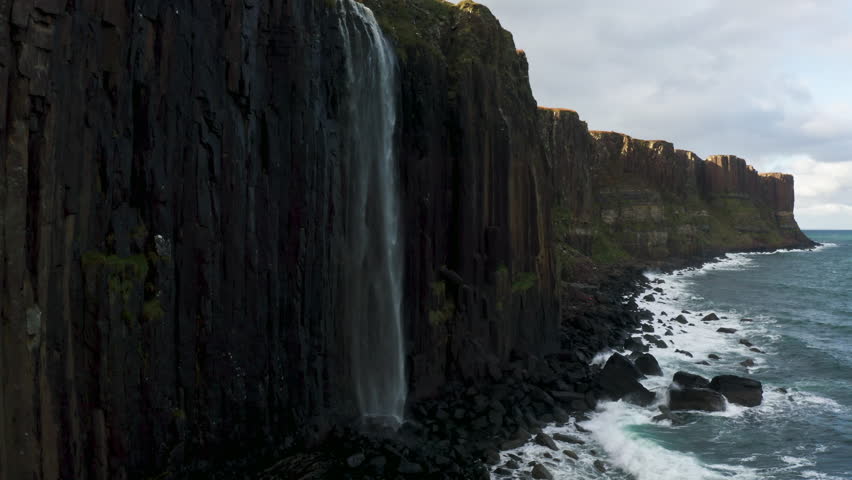 Mealt Waterfall Plunging From Clifftop With View Of Kilt Rock On Isle Of Skye In Scotland, UK. ascending drone shot