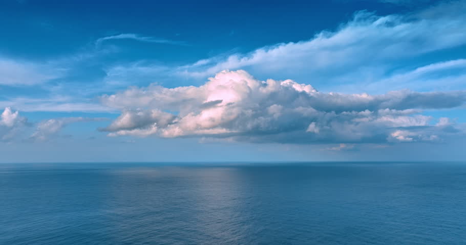 Vast azure waterscape with a beautiful white cloudscape. Bird of prey approaches a drone flying above the rock.