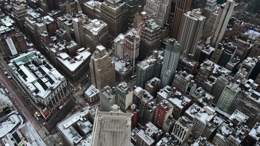 High-angle drone shot slowly looking down at snow-covered rooftops and streets in Manhattan, New York City. Winter scene, urban landscape, establishing shot for NYC, USA