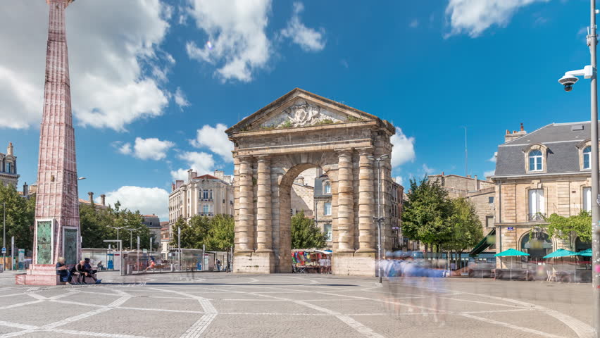 Porte d'Aquitaine arch and obelisk at Place de la Victoire timelapse hyperlapse in Bordeaux, France. Landmark of historic Bordeaux with tram lines, cafes and lively surrounding under blue cloudy sky