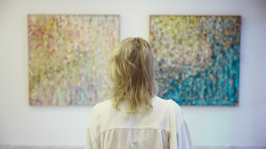 Woman viewed from behind in art gallery, contemplating two abstract paintings on white walls. Modern art exhibition in urban gallery space.
