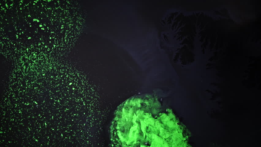 Abstract macro shot of glowing green liquids slowly mixing in dark fluid