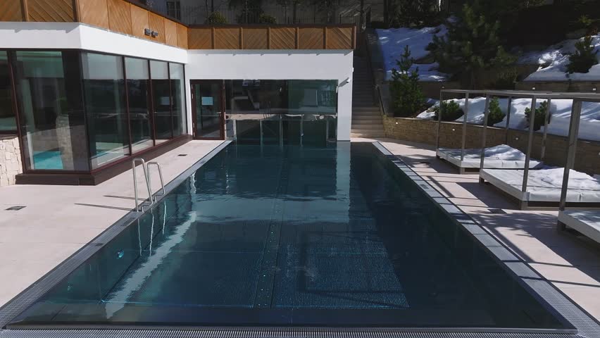 Aerial view of a luxury hotel in Ischgl, Austria, featuring modern architecture, a glass enclosed pool, and snow covered mountainous surroundings.