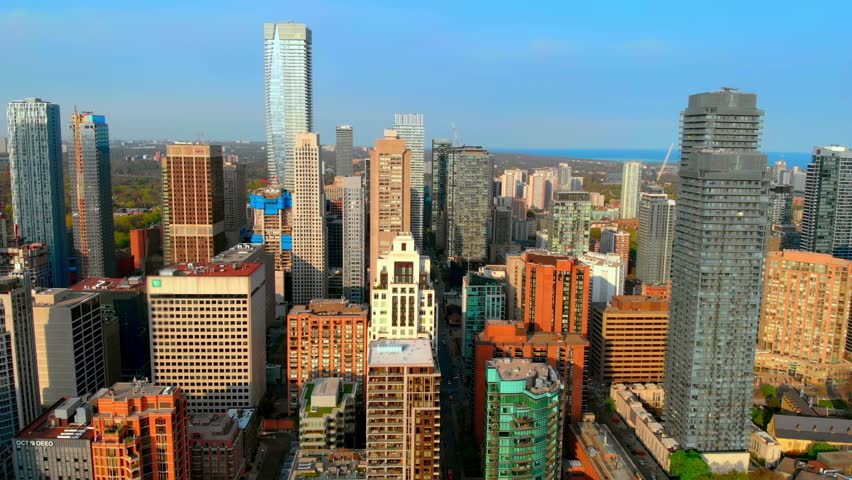Toronto city skyline is displaying a mix of modern and historical architecture, with office towers, residential buildings, and a glimpse of lake ontario in the background under a clear blue sky