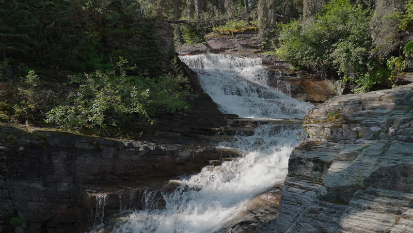 Small waterfall flows over rocky steps, surrounded by lush forest in Montana, USA