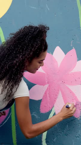 Girl, painting and mural on wall with flowers, smile and art with design for community in urban town. Woman, painter and happy with social responsibility, creative or volunteer for building in Brazil