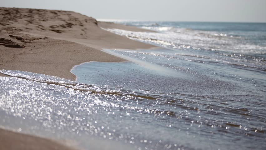 Quiet beach scene with gentle waves meeting smooth, sandy shore. Soft lighting enhances peaceful ambiance. Horizon blends sky and ocean into calming vista