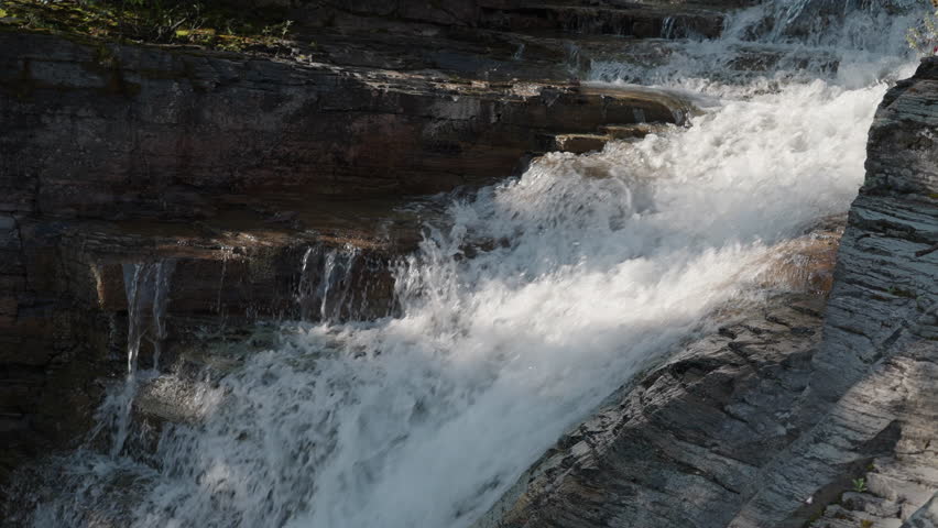 Powerful waterfall crashes over layered rocks in St Mary Falls, Montana, USA