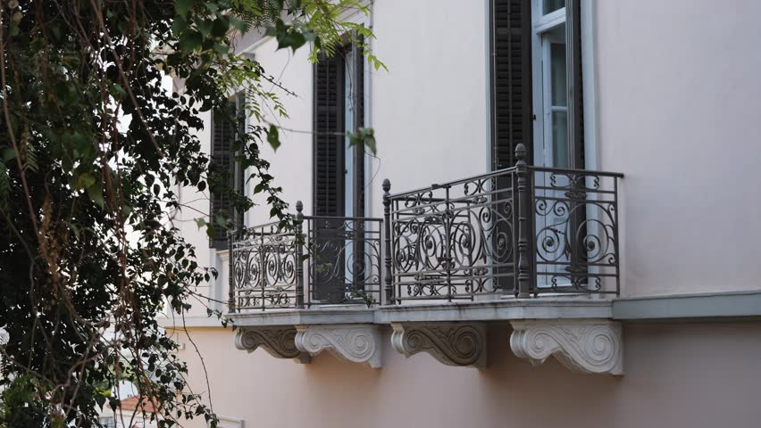 Elegant scene in Athens' old town: two wrought-iron balconies with intricate patterns, open shutters and doors, ornate molding, and a tree to the side. Refined, uncluttered, and full of charm - Powered by Shutterstock - Get 15% off with code: PIKWIZARD15