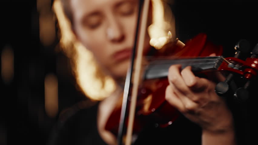 Fabulous sounds of violin, solo of talents female musician, closeup view. Fascinating cinematic details view and portrait, dark and light, rain drops falling in background, slow motion, talented lady