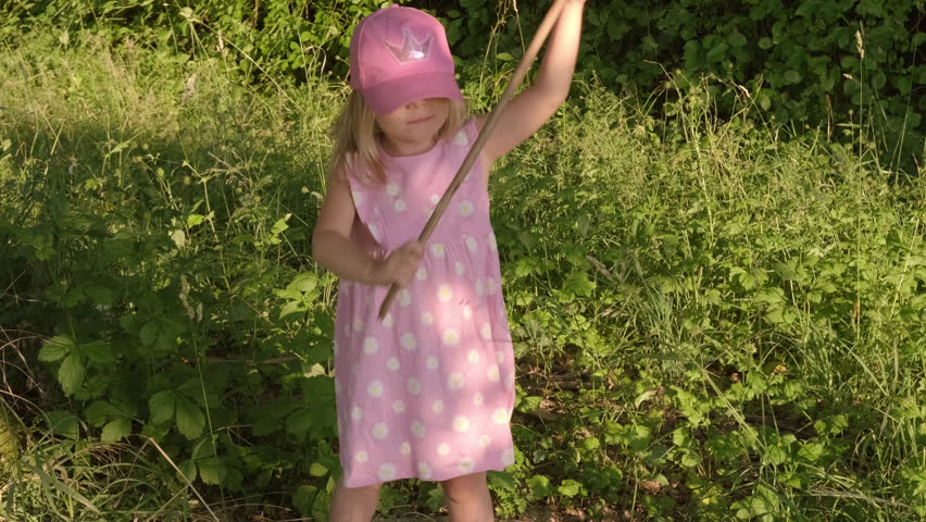 happy cool blonde girl 4 years old in pink dress and cute wreath wildflowers, daisies along old stone road, waves stick, imitates magic wand, do miracles, natural crown on head, wanderer, traveler