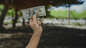 Male hand holding us dollar banknote in a sunny park setting, reflecting currency and casual outdoor financial concept, suitable for finance and lifestyle topics. - Powered by Shutterstock - Get 15% off with code: PIKWIZARD15