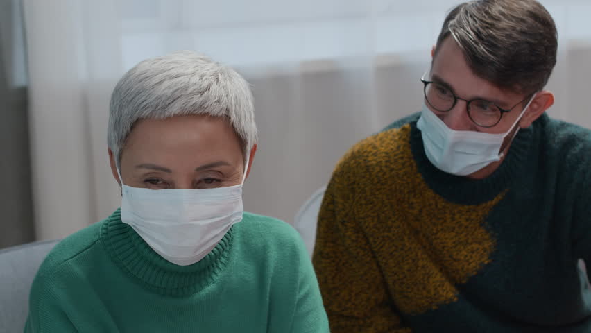 Tilt down shot of wife and son supporting sick man resting in bed in hospital ward