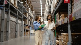Two asian female employees diligent engage in an inventory inspection, with one jotting notes and the other communicating with management via radio in a bustling warehouse filled with packages  - Powered by Shutterstock - Get 15% off with code: PIKWIZARD15