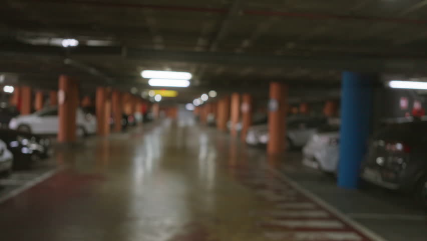 Blurry image of an underground parking lot in soft focus with rows of parked cars and orange and blue columns.