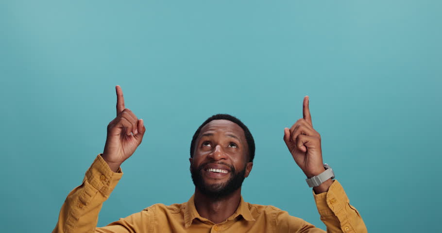 Happy, black man and pointing up with notification in studio for advertising or marketing on a blue background. Portrait, male person or African model with smile for deal, promotion or great offer