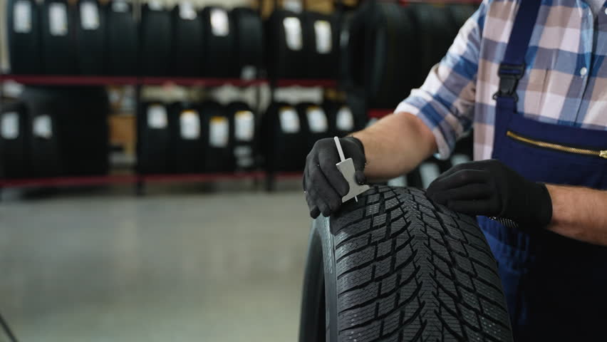 Worker checking tire tread depth with gauge tool