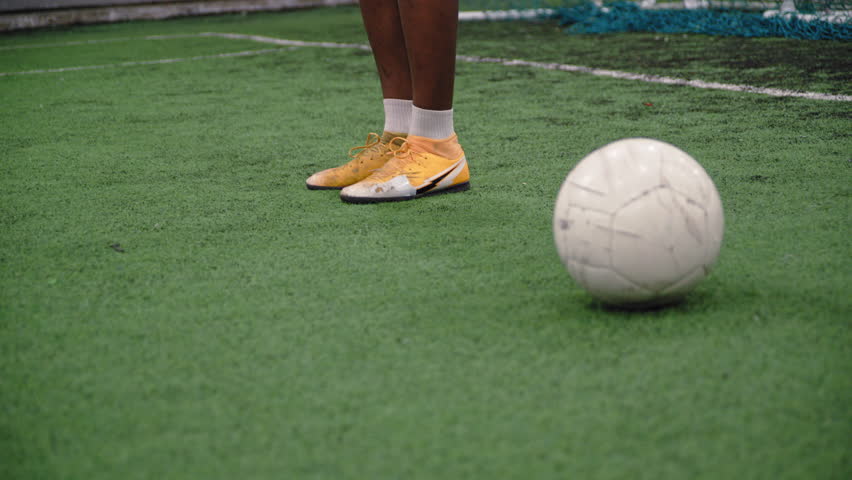 A handheld camera captures a Black football player performing a warm-up routine on the pitch before the match begins.