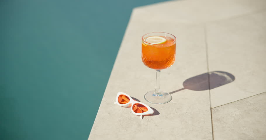 Swimming pool, glass and cocktail with sunglasses for summer vacation, holiday and relax outdoor. Water, alcohol and drink at hotel resort for tourism, travel and luxury with fresh lemon beverage